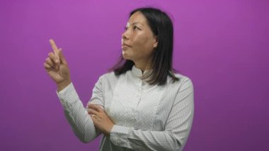 Kadın işaret parmağı yukarı doğru çapraz kol ve beyaz çizgili gömlek ile mor stüdyoda; özgüven odaklı.