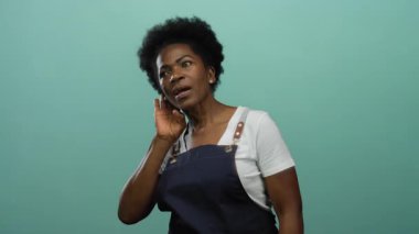 Önlüklü kadın yeşil arka planda dikkatle dinliyor, merak ve nişan gösteriyor..