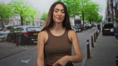 Şehir caddesinde, kahverengi tişörtlü ve uzun saçlı, hafifçe sırıtan ve el hareketlerini yükselten bir kadın..