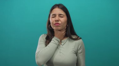 Genç İspanyol kadın yeşil bir stüdyoda boğazı ağrıdığı için iki eliyle boğazını tutuyor..