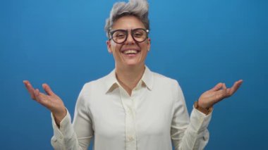 Kısa saçlı, gözlüklü, gözleri gölgeleyen ve stüdyoda gülümseyen beyaz bir kadın..