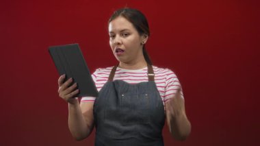 Kırmızı stüdyoda kot önlük giyerken tek eliyle ve alnından tablet tutan kadın hayal kırıklığı teknisyeni sorunu.