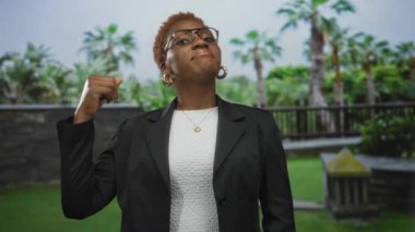 Kadın, yeşil ağaçların ve ormandaki palmiyelerin arasında hafif bir sırıtışla ceketini düzeltir..