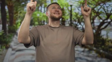 Adam gülüyor ve her iki işaret parmağı yukarı görünür eller ve ön kollar ile ağaçlar ve yol arasında bir orman geçidi üzerinde; umut zafer.