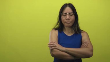 Mavi elbiseli ve kolları çaprazlanmış bir kadın limon yeşili stüdyo ortamında nişan yüzüğü gösteriyor..