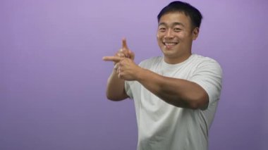 Beyaz tişört giyen genç Çinli adam gülümsüyor ve parmağıyla mor stüdyoyu işaret ediyor..