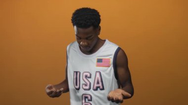Beyaz basketbol formalı adam, turuncu stüdyoda avuç içi ve bakışlarını hafifçe aşağıya doğru uzatıyor; belirsizlik..