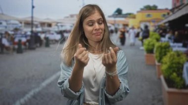 Genç sarışın kadın, canlı bir sokak pazarında avuç içine parmak hareketiyle para hareketi yapıyor..