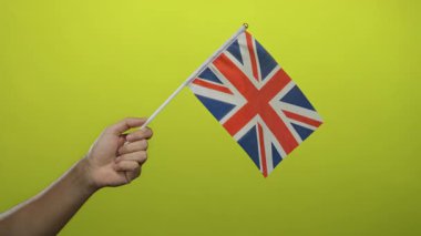 Canlı ve izole bir ortamda vatanseverlik ve milliyetçilik gösteren canlı sarı arka plana karşı İngiliz bayrağı tutan adam..