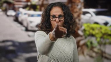 Şehirde kıvırcık saçlı, gözlüklü ve hırkalı bir kadın ciddi bir ifade takınıyor..