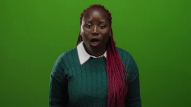 Afrikalı Amerikalı kadın canlı, izole edilmiş yeşil bir arka plana karşı jestler yapıyor. Duygularını ve iletişimini vurguluyor..