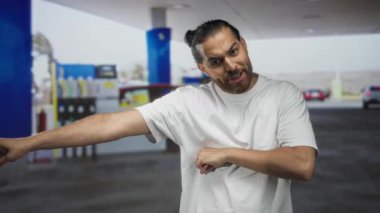 Geniş kollu ve kollu bir adam caddenin ön pervazında benzin pompası ile çapraz; öfke yüzleşme gerilimi.