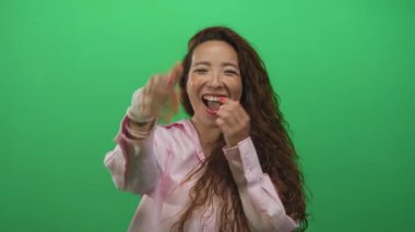Pembe tişörtlü, elleri yanaklarında ve ağzı açık gülümseyen yeşil stüdyoda gülen bir kadın. Sürpriz sevinç sıcaklığı..