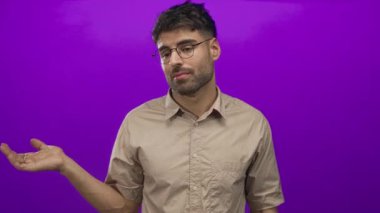 Gözlük takan ve hafif gülümseyen bir adam, parlak mor stüdyoda avucunun içini işaret ediyor..