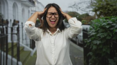 Elleri kafasında, ağzı açık, gözlük takan bir kadın çığlıkta şehir evleriyle dolu bir caddede dikilirken hayal kırıklığına uğradı..