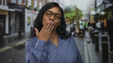 Mavi bluz giyen ve gözlüklü bir kadın gün ışığında dudaklarıyla öpücük yolluyor..