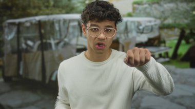 Gözlüklü genç adam, kampçı tarafından desteklenen yeşil parktaki caddede kamerayı işaret ediyor..