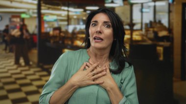 Restoranın içinde, yüzüklü ellerle yüzünü koruyan kadın kareli zeminde yeşil bluz giyiyor, reddediliyor..