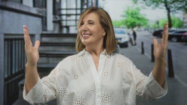 Kadın kalabalık şehir caddesinde geniş açık kollarını tutuyor, avuçlar önde geniş gülümseyerek; neşe açıklığını sıcak karşılıyor.