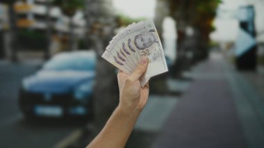 Şehrin arka planında bulanık arabalı ve şehir içi ve para birimi detaylarını vurgulayan Singapur Doları 'nı elinde tutan adam.