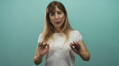 Elleri havada ve gözleri kapalı bir kadın stüdyoda turkuaz arka planlı beyaz tişört giyiyor; sakin meditasyon.