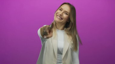 Kadın kendinden emin bir şekilde neşeli bir gülümsemeyle parlak pembe bir arka plana işaret ederek çekici bir gençlik havası yaratıyor.