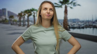 Güneşli bir günde, arka planda palmiye ağaçları ve denizle kumsalda güven içinde duran genç bir kadın..