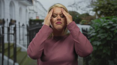 Sarışın kadın, şehrin dışındaki evin girişinde demir parmaklıklarla tapınaklara el ele tutuşuyor. Stres..