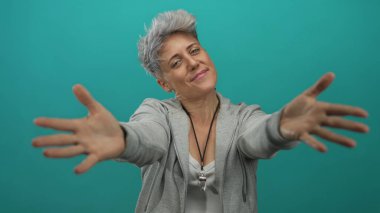 Gülümseyen kısa saçlı kadın elleriyle omuzlarını sarmalıyor. Stüdyo duvarına yaslanıyor..