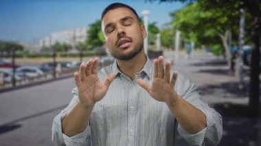 Açık mavi çizgili tişörtlü genç İspanyol adam kalabalık şehir caddesinde durmak için iki elini de açık tutuyor..