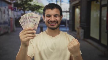 Gülümseyen adam Suudi riyal banknotlarını elinde tutuyor ve işlek şehir caddesinde yumruk sallıyor; finansal başarı.