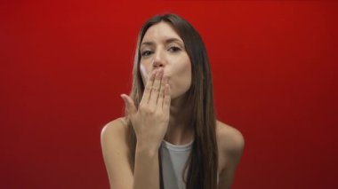 Genç İspanyol bir kadın canlı kırmızı bir stüdyo arkaplanına el pençe dize öpüşüyor..