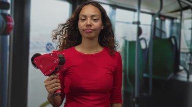 Otobüs koridorunda kırmızı bluz giyerken sağ elinde bant paketleyicisi tutan kadın..