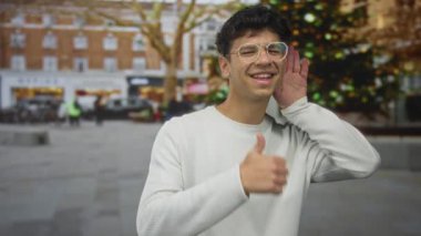 Bir adamın tek eliyle kulağını kavraması ve bir şehir caddesinde baş parmak işareti göstermesi; iletişim bağlantısının onaylanması teşvik edici.
