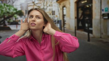 Pembe tişörtlü kadın canlı bir şehir caddesinde arka planı bulanık bir şekilde dikkatlice dinliyor, şehir merkezindeki şehir enerjisini ve merakını yakalıyor..