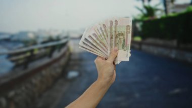 Açık bir sokak ortamında Rus rublesi banknotları tutan, döviz kurunu veya ekonomik konsepti finansal unsurlar ve kentsel çevre üzerine odaklı gösteren bir adam.