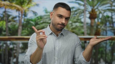 Palmiye uzatan ve yeşil parkta parmağını sallayan adam tropik yapraklı palmiye ağaçlarının altında tereddüt ediyor..