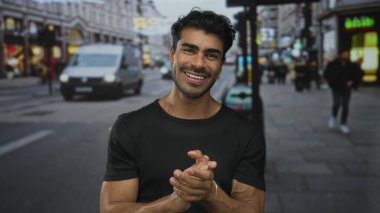 Mağazalar ve gün ışığında geçen araçlarla dolu kalabalık şehir caddesinde el çırpan adam;.