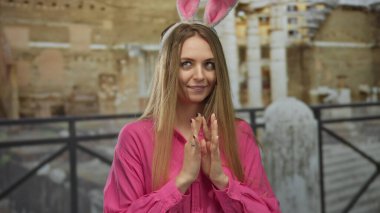 Pembe tişörtlü ve tavşan kulaklı bir kadın, eski bir kasaba caddesinde neşeli mizacını, tarihi bir şehrin arka planına karşı sergiliyor..