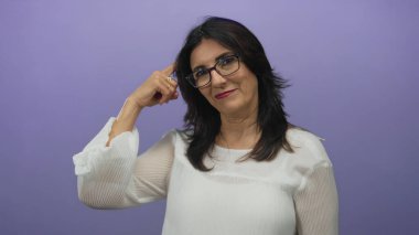 Orta yaşlı, gözlüklü ve beyaz bluzlu İspanyol kadın stüdyoda parmak ucuyla tapınağı işaret ediyor..