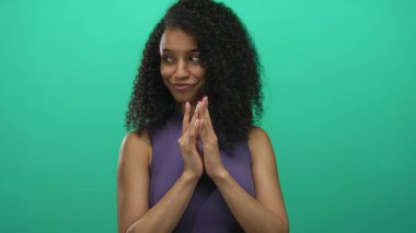 Genç bir kadın, izole edilmiş, parlak yeşil bir geçmişe karşı muzip bir jest yapıyor. Etkileyici gözleriyle entrika ve duygunun unsurlarını vurguluyor..