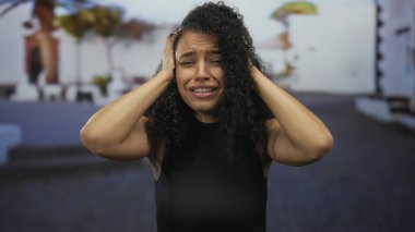 Kadın, güneşli bir sokakta kendini stresli hissediyor. Kafasını ellerinin arasına almış Latin kökenli genç bir kadın, hayal kırıklığını dile getiriyor..