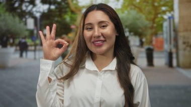 Latin kökenli genç bir kadın, şehir merkezindeki ağaçlarla çevrili caddede gün batımında el ele tutuşuyor..