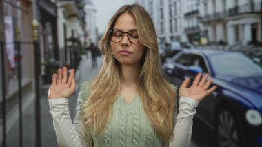 Sarışın kadın çıplak ellerini kaldırır ve başını eğik bir şekilde şehir sokaklarında dikkatsizlik eder..