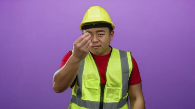 Asyalı bir adam para için inşaat malzemeleri giyer canlı mor bir geçmişe karşı jest yapar, finansal istek ve müzakere ifadesini yakalar..