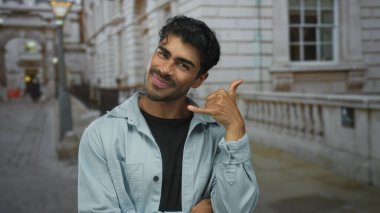 Genç Hispanik adam, meşgul bir şehir sokak ortamında bana el hareketleriyle şakacı çağrı yapar; dostça bir davet.