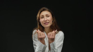 Duygularını ifade eden kadın, elleri izole edilmiş siyah arka plan üzerinde, beyaz gömlek giyiyor, güçlü görsel unsurlara sahip net ve etkili bir mesaj iletiyor ve yoğun bir şekilde odaklanıyor..