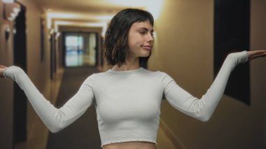 Yorgun genç İspanyol kadın, sıcak aydınlatma altında bir otel koridorunda omuz silkiyor..
