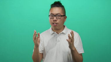 Yeşil bir stüdyoda el kaldırarak el kol hareketi yapan beyaz polo ve gözlük takan bir adam hayal kırıklığı odaklı düşünce.