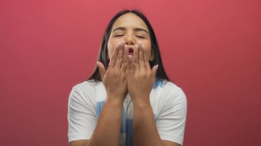 Genç bir kadın, canlı kırmızı bir arka plana gülümserken öpücükler savuruyor, sıcaklık ve neşe taşıyor..